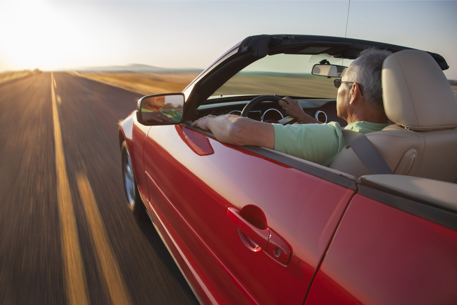 A senior Hispanic man at the wheel of his convertible sports car at sunset