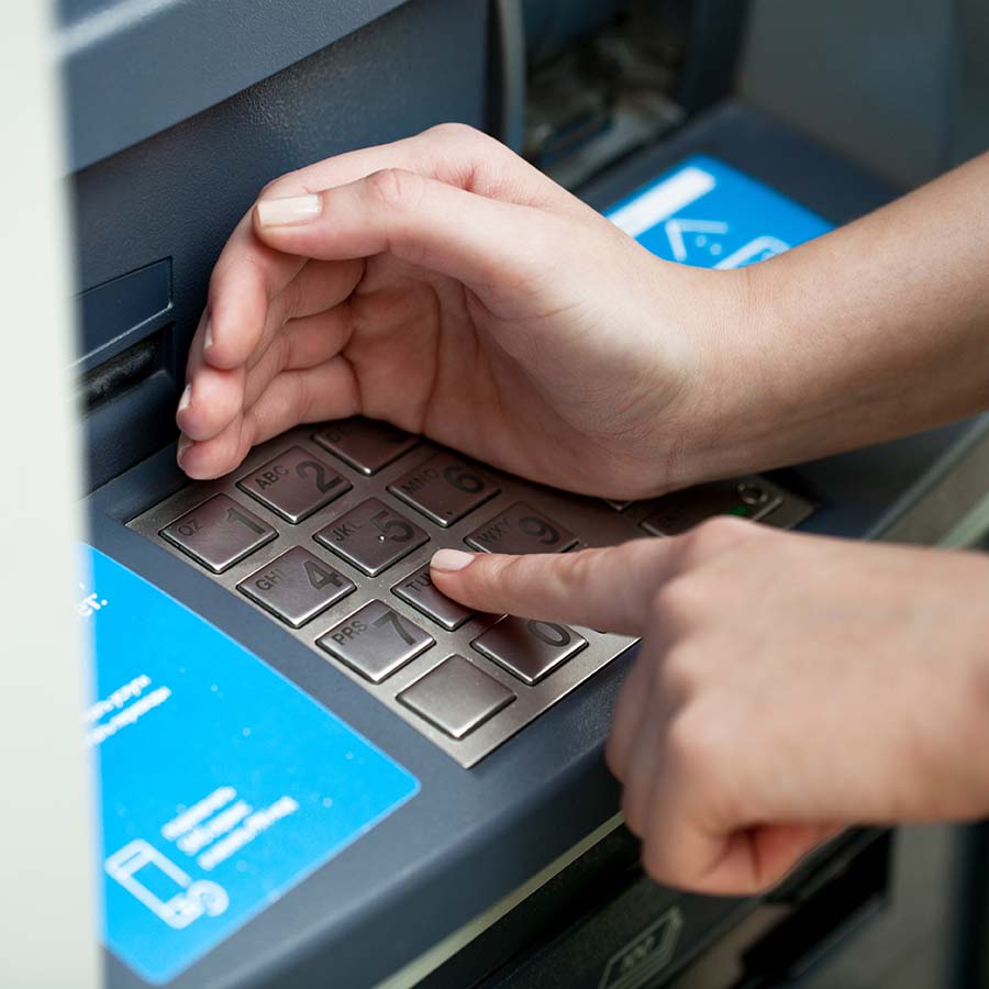 Person covers pin pad with hand as they enter their pin number at an ATM.