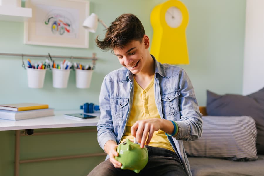 A teen boy puts money into his piggy bank.