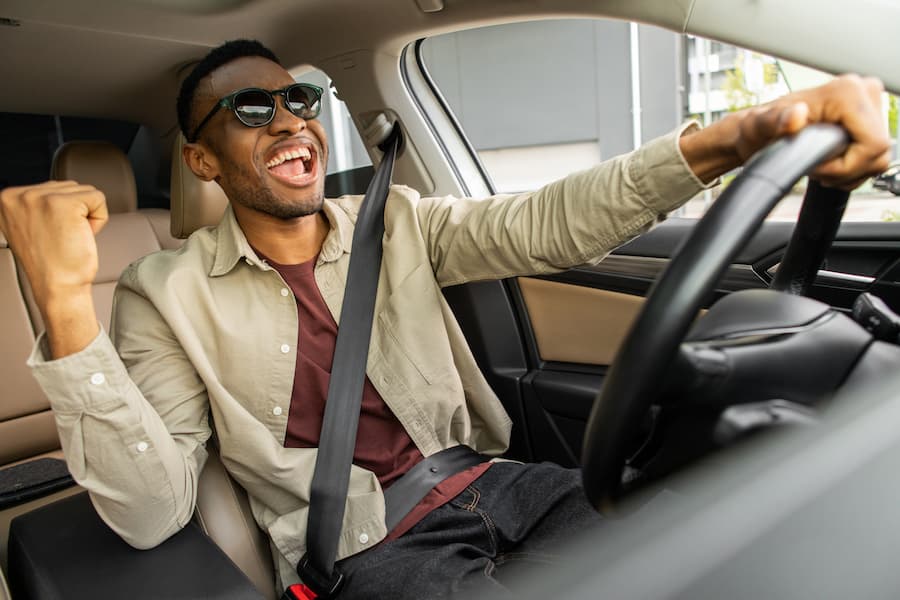 A black man joyfully sitting in the driver's seat of his new car.